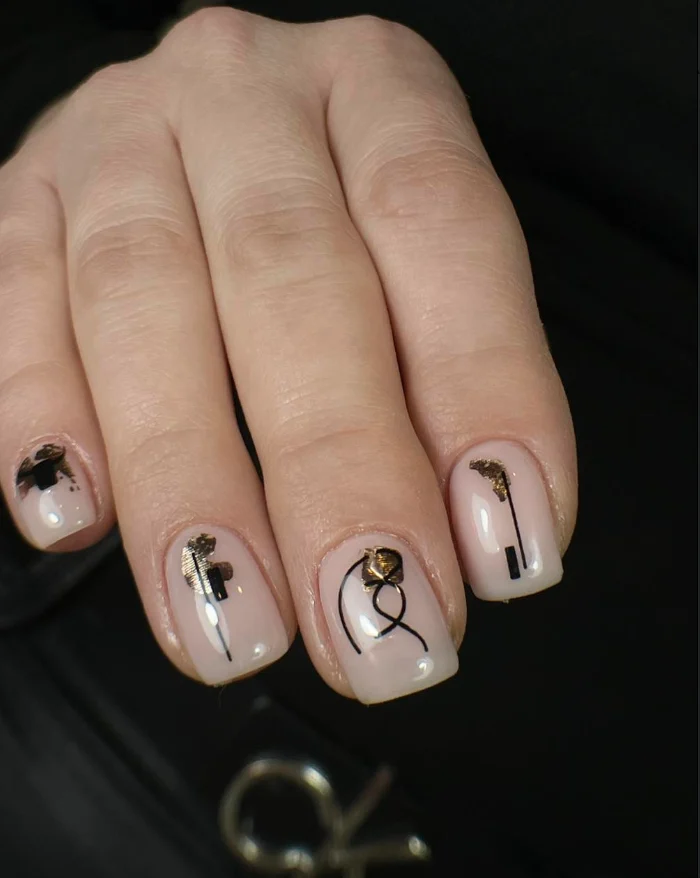 Nail art nude avec traits noirs et éclats dorés, sur fond noir