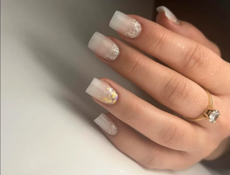 Main aux ongles carrés nude et paillettes, bague dorée
